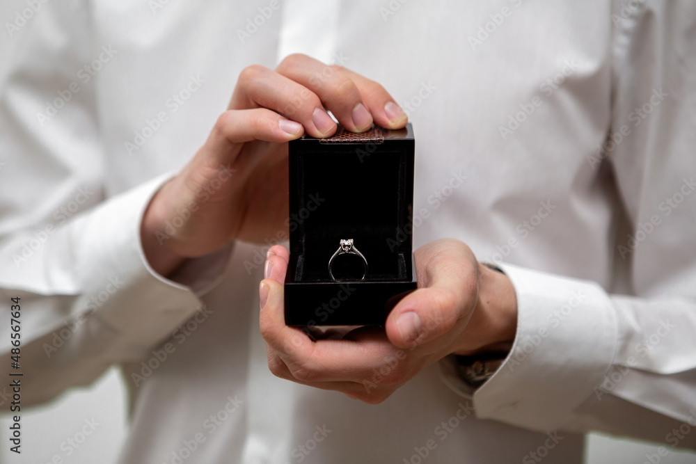 A young man holds in his hands a jewelry box with a diamond ring inside A young man holds in his hands a jewelry box with a diamond ring inside