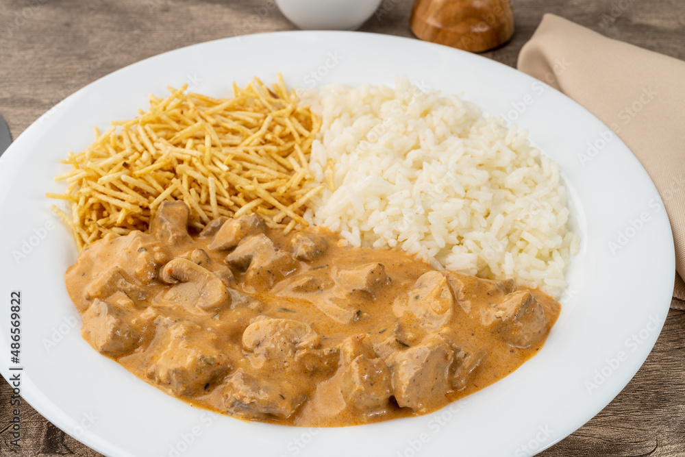 Meat strogonoff with rice and straw potato over wooden table Meat strogonoff with rice and straw potato over wooden table