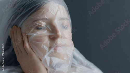 A blonde teen girl breathes through polyethylene and suffocates, cannot breathe through a bag, close up, hand on face