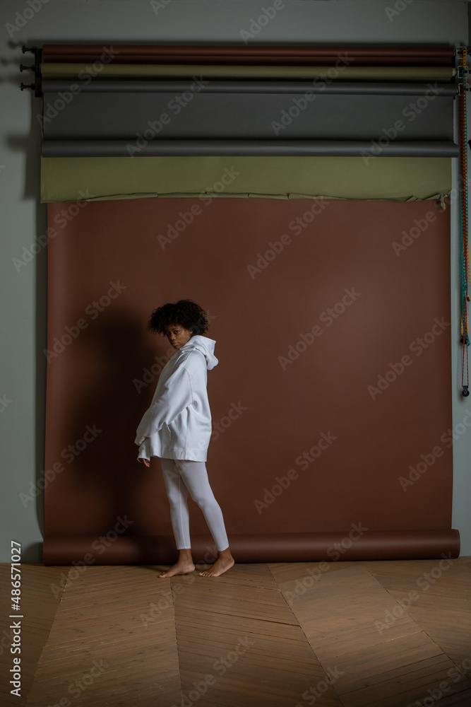 African american woman in a white hoodie and leggings stands on a brown background. Mock-up. African american woman in a white hoodie and leggings stands on a brown background. Mock-up.