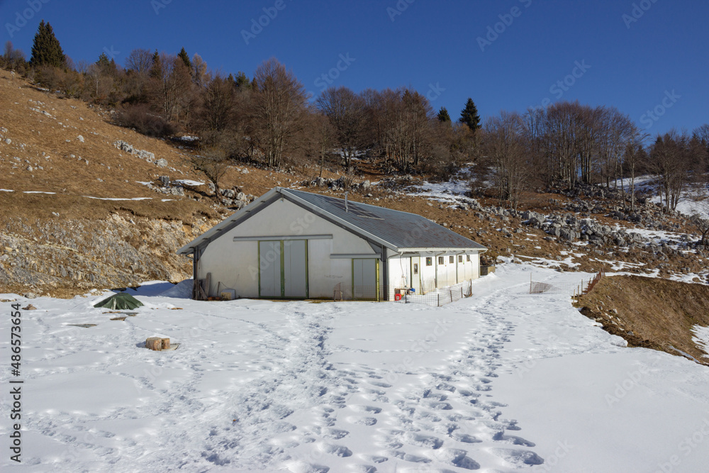 Winter landscape. A white stable in the middle of the rocks and the woods. Footprints of people in the snow.
