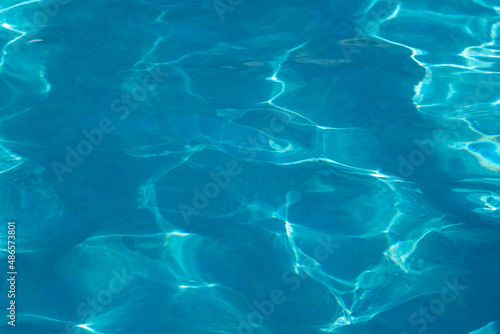 Blue background of clean transparent water. Natural water texture. Beautiful pattern of sun glare on the water surface. The nature of the sea.
