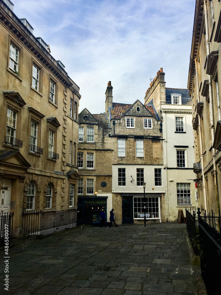 Medieval architecture in Bath, England. Stone houses, different shape of windows, cobbled street. Blue sky. Name of the area is written on the left side - “North Parade Blds”