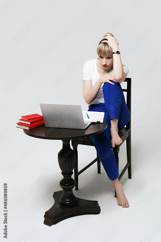 Focused young female student sitting at desk working or studying remotely online writing notes while looking on laptop screen. Distant learning or remote work from home. Isolated on white background.