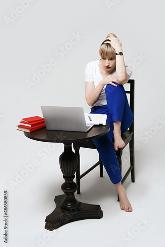 Focused young female student sitting at desk working or studying remotely online writing notes while looking on laptop screen. Distant learning or remote work from home. Isolated on white background.