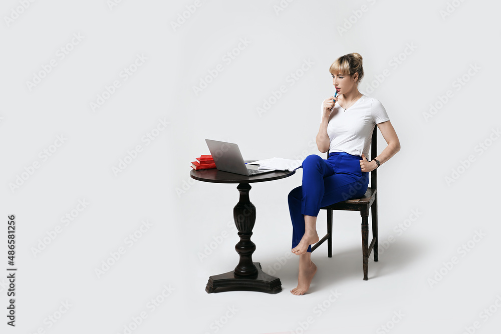 Thoughtful young female student sitting at desk working or studying remotely online looking on laptop screen with interest biting pen and thinking. Distant learning or remote work from home.