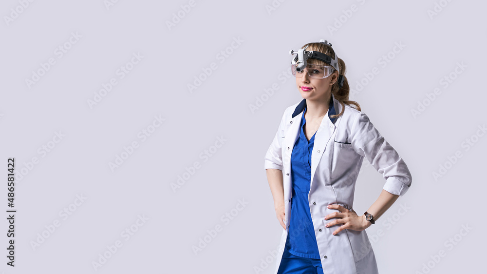 Confident ENT doctor wearing surgical headlight head lantern and protective glasses. Portrait of female otolaryngologist or head and neck surgeon on light grey background.