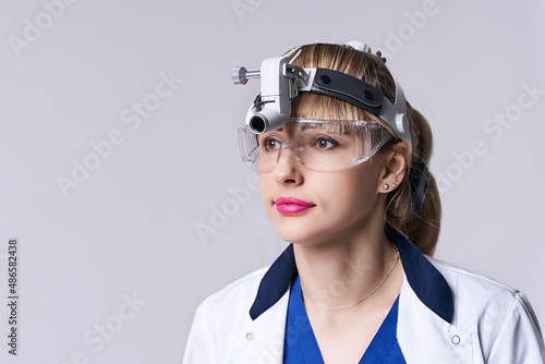 Obraz na płótnie Confident ENT doctor wearing surgical headlight head light and protective glasses. Closeup portrait of female otolaryngologist or head and neck surgeon on light grey background. w salonie