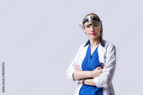 Obraz na płótnie Confident ENT doctor wearing surgical headlight head light and protective glasses. Portrait of female otolaryngologist or head and neck surgeon standing arms crossed on light grey background. w salonie