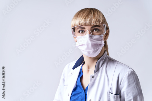 Obraz na płótnie Confident blonde female doctor wearing protective face mask. Portrait on light grey background. w salonie