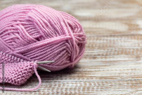 Knitting with needles and pink yarn skein on wooden background, horizontal, copy space