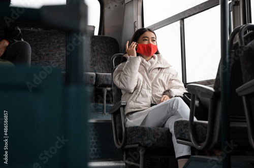 Asian woman putting on mask during bus ride photo