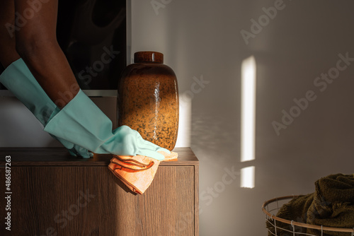 Crop housewife wiping dust near vase