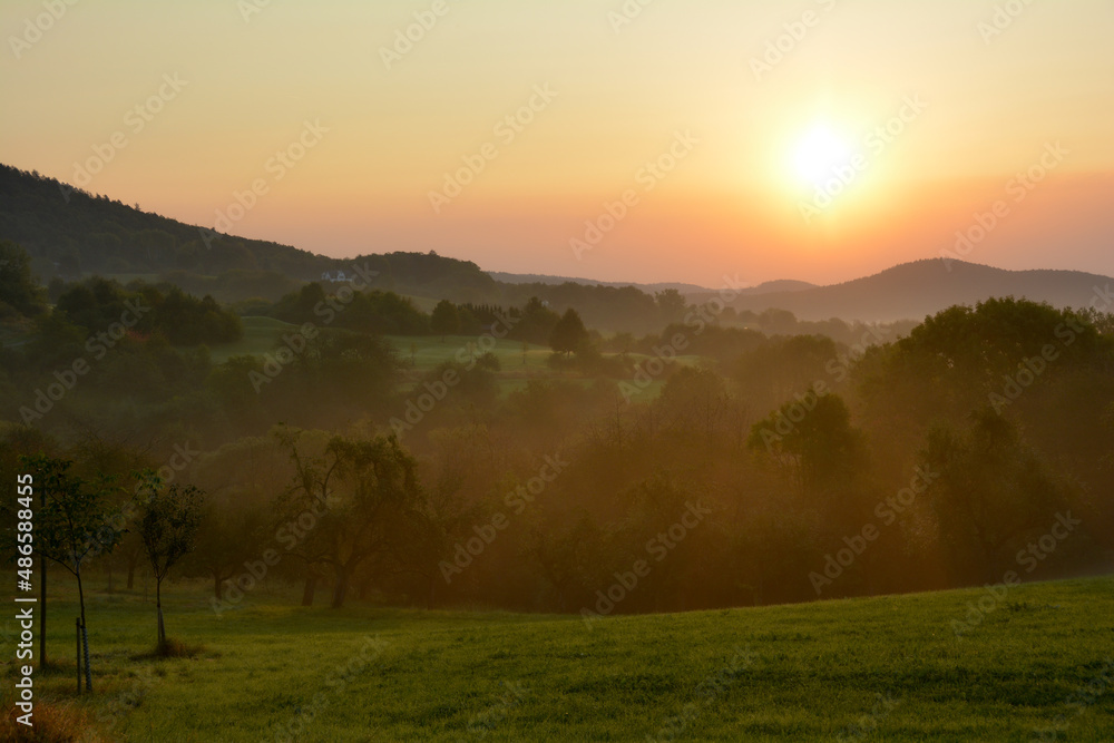 Fototapeta premium Sun rises over a landscape with morning fog