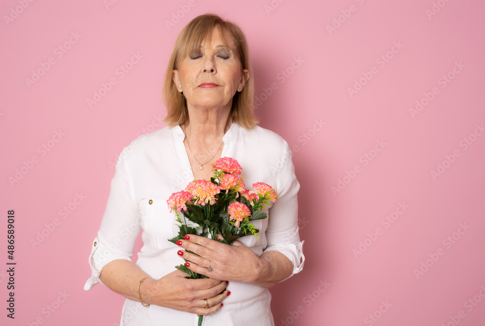 Happy senior woman holding bouquet of flowers with closed eyes isolated over pink background. Happy senior woman holding bouquet of flowers with closed eyes isolated over pink background.