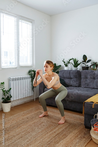 Sportive woman practicing squat at home photo