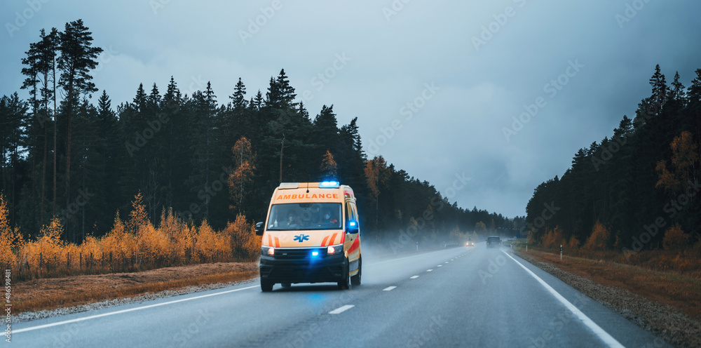 Defocused photo of ambulance car on the highway, blurred image of an emergency car running on the forest road at the cloudy evening Defocused photo of ambulance car on the highway, blurred image of an emergency car running on the forest road at the cloudy evening