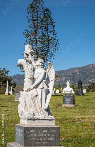 Santa Barbara  California  USA - February 8  2022  Calvary Cemetery. Closeup of white stone Edmund Arellanes unique historic tombstone on green burial lawn under blue sky. Tall tree