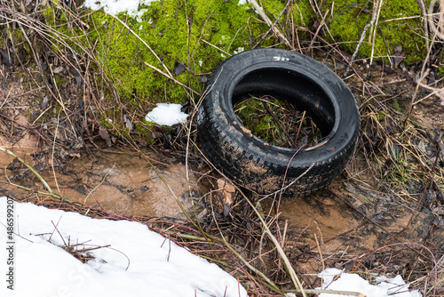 Random garbage junk items left in nature. Old tire in the ditch on winter day.