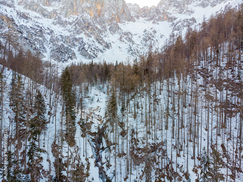 Spectacular aerial view of frozen waterfall falling over rocky ledge during winter.