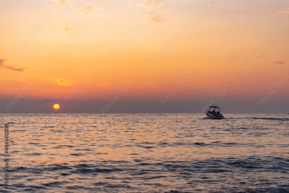 Sunset on the sea with a boat. The sun sets behind the sea horizon, and the boat sails into the sunset.
