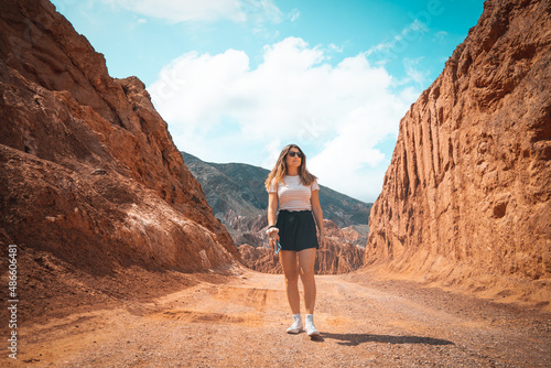 Wide angle view of a caucasian woman walking and holding her mobile phone on a mountain road.