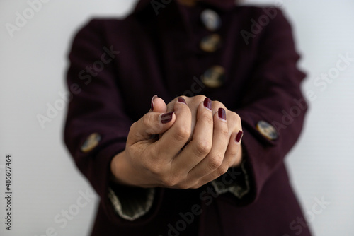 Portrait of young Latin American woman (22) showing her hands in the foreground, wearing a purple coat. Gray background.