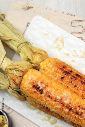 Grilled Sweet Corn with Butter and Shredded Mozarella. Served on White Plate