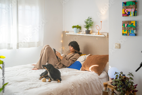 Asian Woman Laying On The Bed And Studying With Her Dog photo