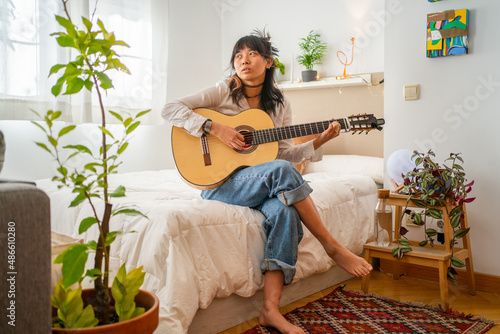 Asian Woman Playing The Guitar In Her Bedroom At Home.