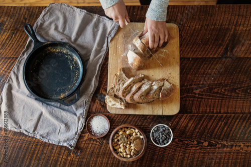 A woman cuts whole grain sourdough bread on a rustic wooden surface.