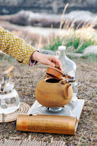 A woman checks on the water of a tea pot during a tea ceremony outside by the river.