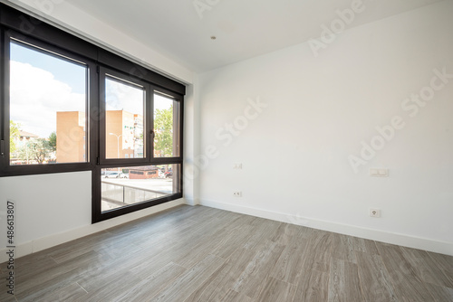 Newly renovated empty room with large black aluminum window and views of the city with imitation wood stoneware floor