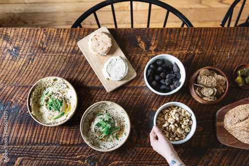 A variety of vegan snacks and appetizers on a rustic wooden table with a hand holding one bowl.
