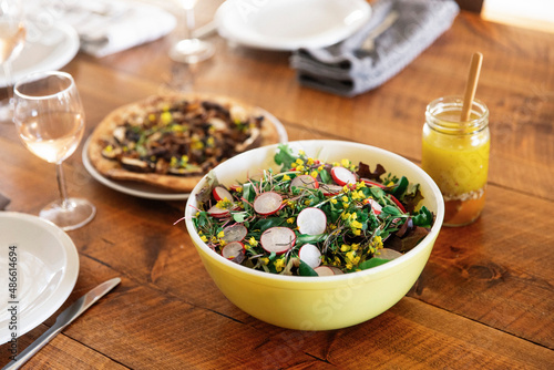A garden salad in a yellow bowl on a rustic wooden table.