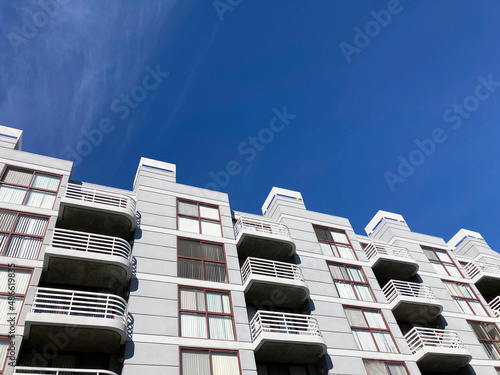 Exterior view of typical multifamily mid-rise residential apartment building with balconies and identical windows blinds under blue sky