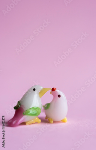pareja de pájaros de juguete miniatura dándose un beso, un piquito. con fondo rosado 