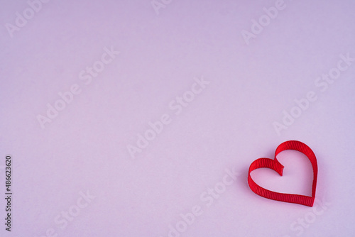 Top view Valentine's Day concept with copy space. Red ribbon heart on purple papper background photo