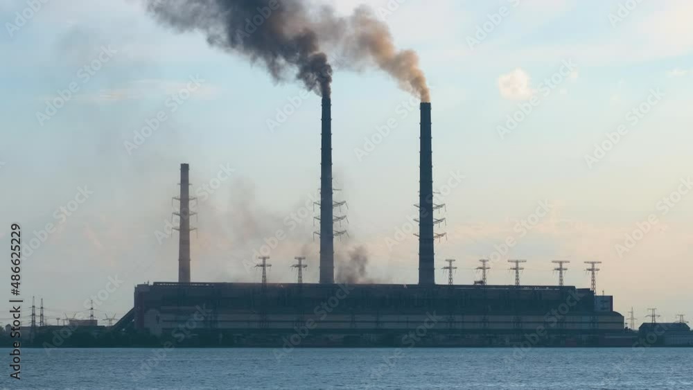 Coal power plant high pipes with black smoke moving upwards polluting atmosphere over lake water Coal power plant high pipes with black smoke moving upwards polluting atmosphere over lake water