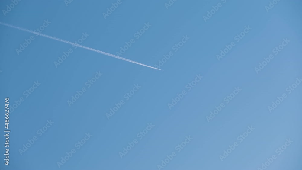 Distant passenger jet plane flying on high altitude on clear blue sky leaving white smoke trace of contrail behind. Air transportation concept Distant passenger jet plane flying on high altitude on clear blue sky leaving white smoke trace of contrail behind. Air transportation concept