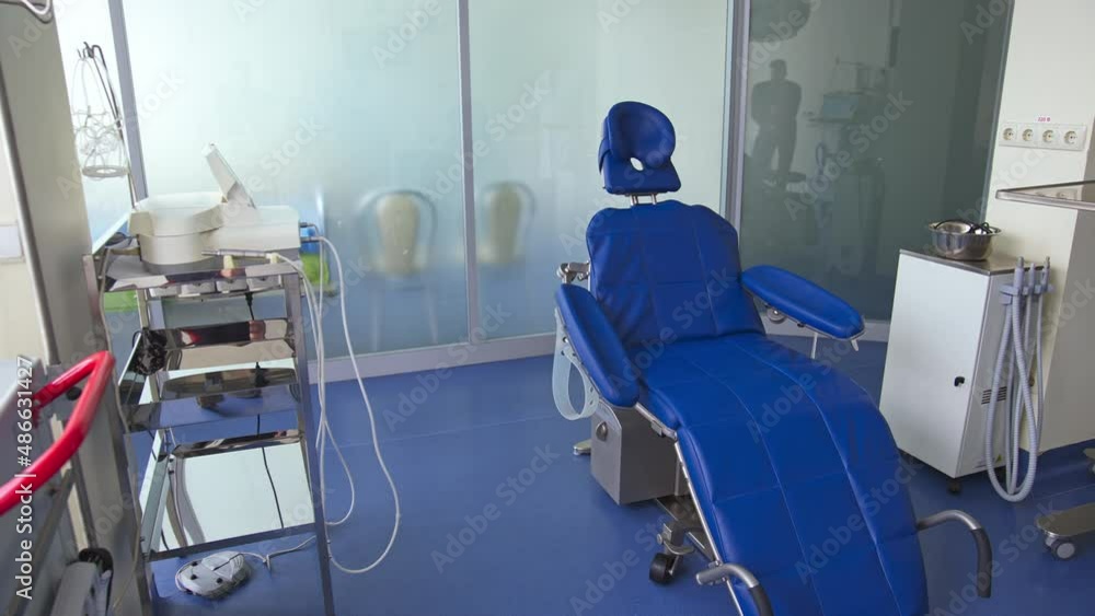 Blue comfortable folding chair in dentist’s cabinet. Light room with diverse equipment for stomatological purposes. Blue comfortable folding chair in dentist’s cabinet. Light room with diverse equipment for stomatological purposes.