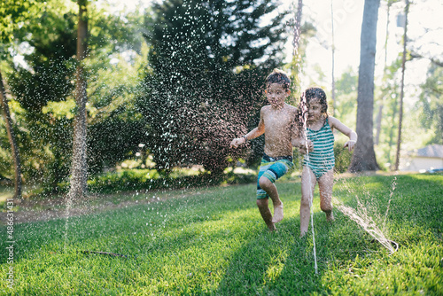 Young siblings playing in a sprinkler photo