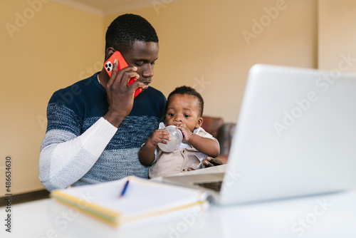 Black dad with toddler speaking on cellphone photo