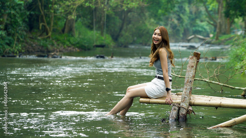Fototapeta Naklejka Na Ścianę i Meble -  Happy young asian woman sitting near the stream, smiling and looking to the camera in the forest, enjoy traveling on holidays.