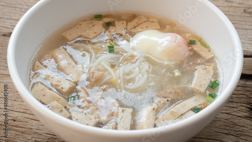 Close-up Vietnamese Rice Noodles Soup with soft-boiled eggs and parsley in white bowl on wooden table background