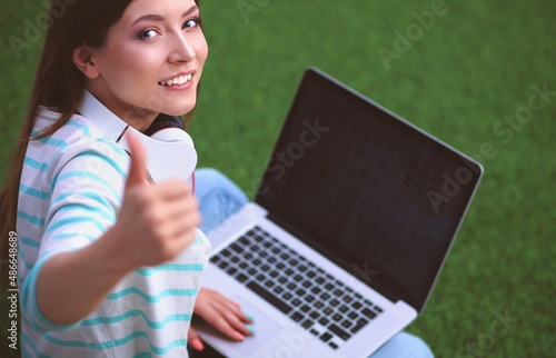 Young woman with laptop sitting on green grass