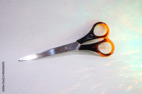 Metal scissors with orange-brown rings on a light background with backlight