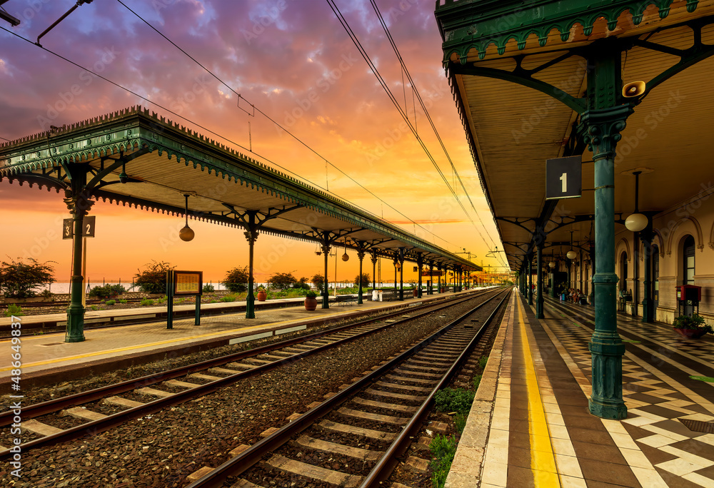 beautiful vintage railway station with platforms with nice roofs and tracks, leadiga far away into sunset , cityscape with amasing background
