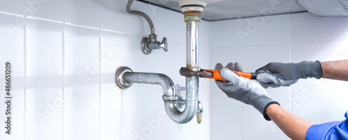 Foto Technician plumber using a wrench to repair a water pipe under the sink