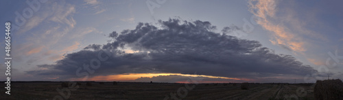 Panorama of a mown field against the background of a menacing sky at sunset